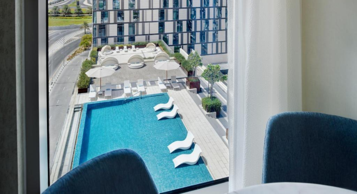 View of outdoor swimming pool at Staybridge Suites Dubai Al-Maktoum Airport with sun loungers and modern hotel surroundings