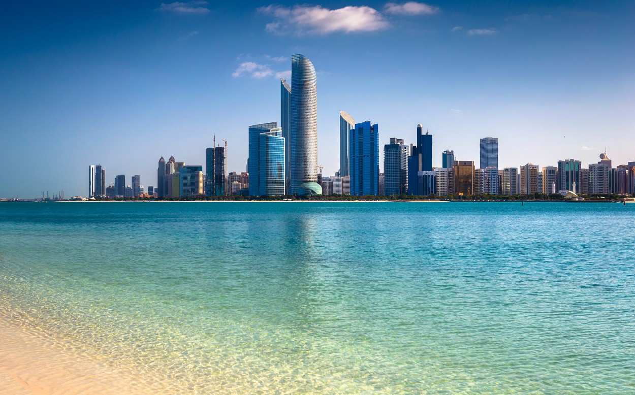 City skyline with tall modern buildings by a clear blue shoreline