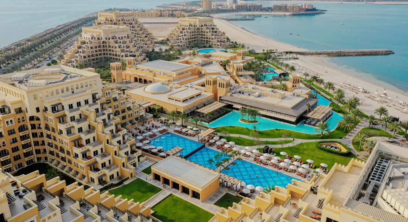 Aerial view of a large beachfront resort with pools, gardens, and sandy shoreline