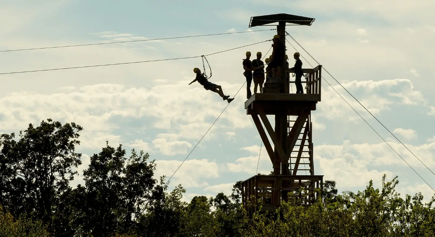 Person ziplining from a tall wooden platform with trees and sky in the background