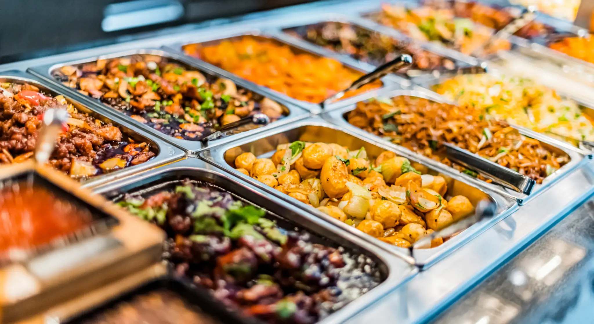 Assorted hot dishes and curries in a luxury buffet counter at a hotel restaurant with stainless steel serving trays.