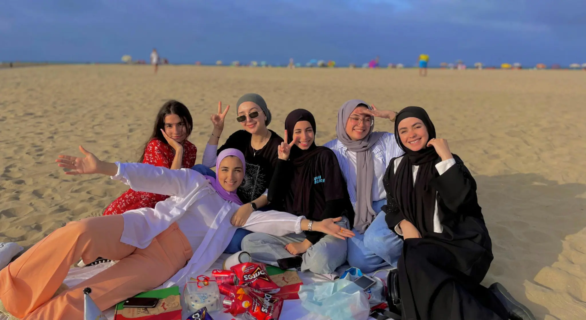 Group of friends relaxing on beach in Dubai with picnic and sunset sky