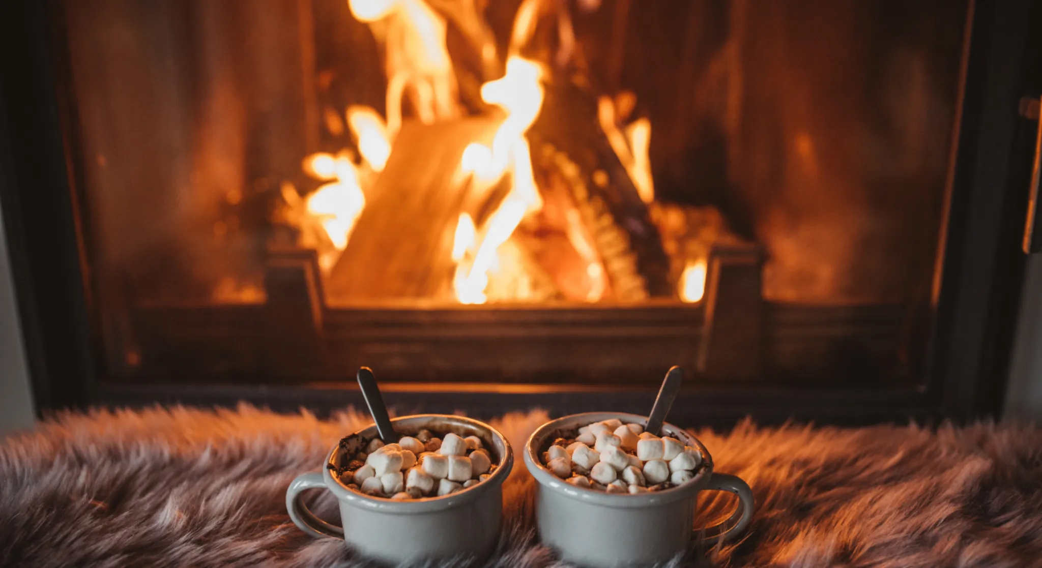 Cosy winter scene with hot chocolate and marshmallows by a fireplace, representing warm seasonal stays and winter travel comfort .