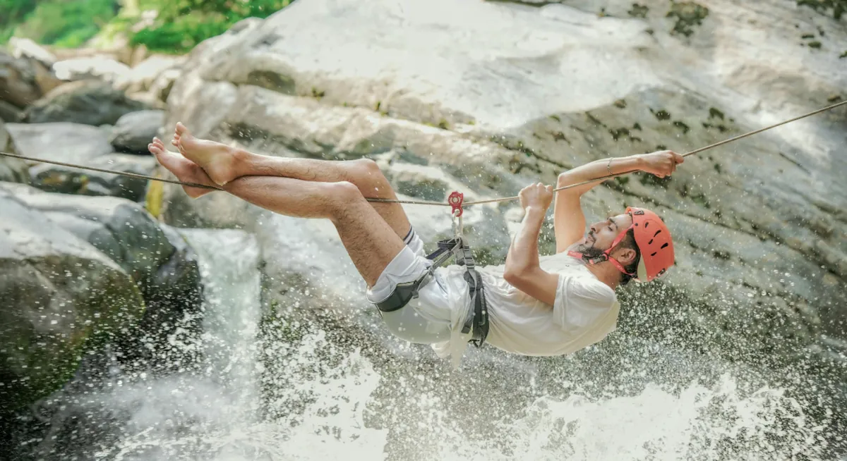 Man ziplining over a rocky waterfall at Jebel Jais, Ras Al Khaimah, showcasing weekend adventure activities near Dubai.
