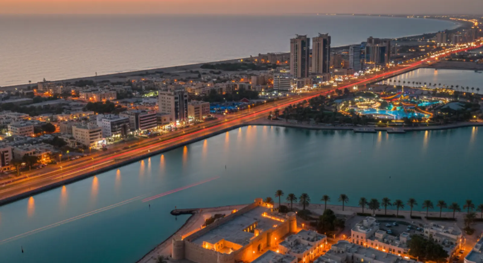 Aerial night view of UAE coastal city skyline with waterfront and highway lights/