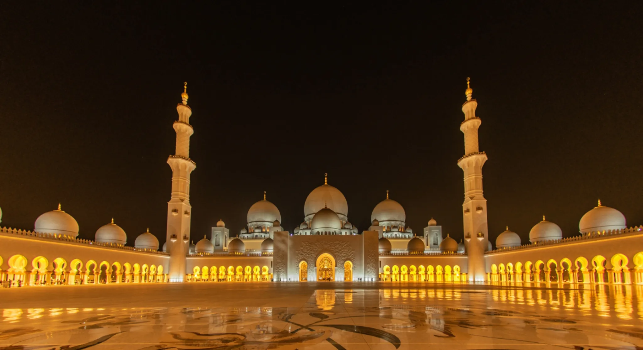Sheikh Zayed Grand Mosque Abu Dhabi illuminated at night with glowing arches and domes.