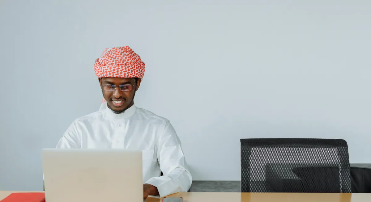 Woman in hijab shopping online from sofa using phone and laptop at home.