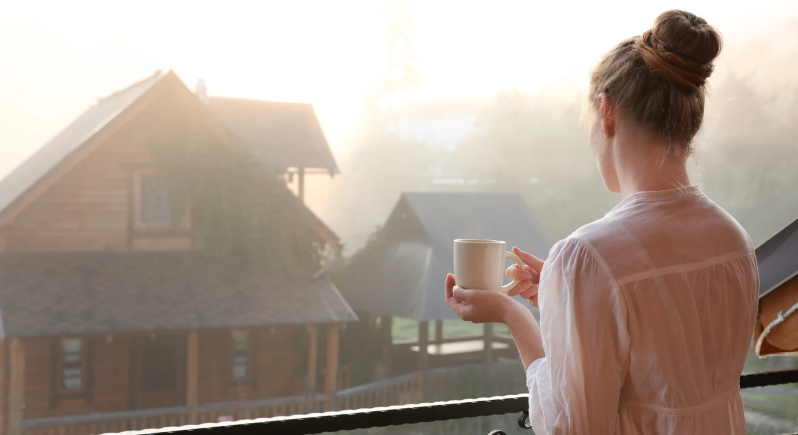 Woman holding coffee on balcony during early morning light