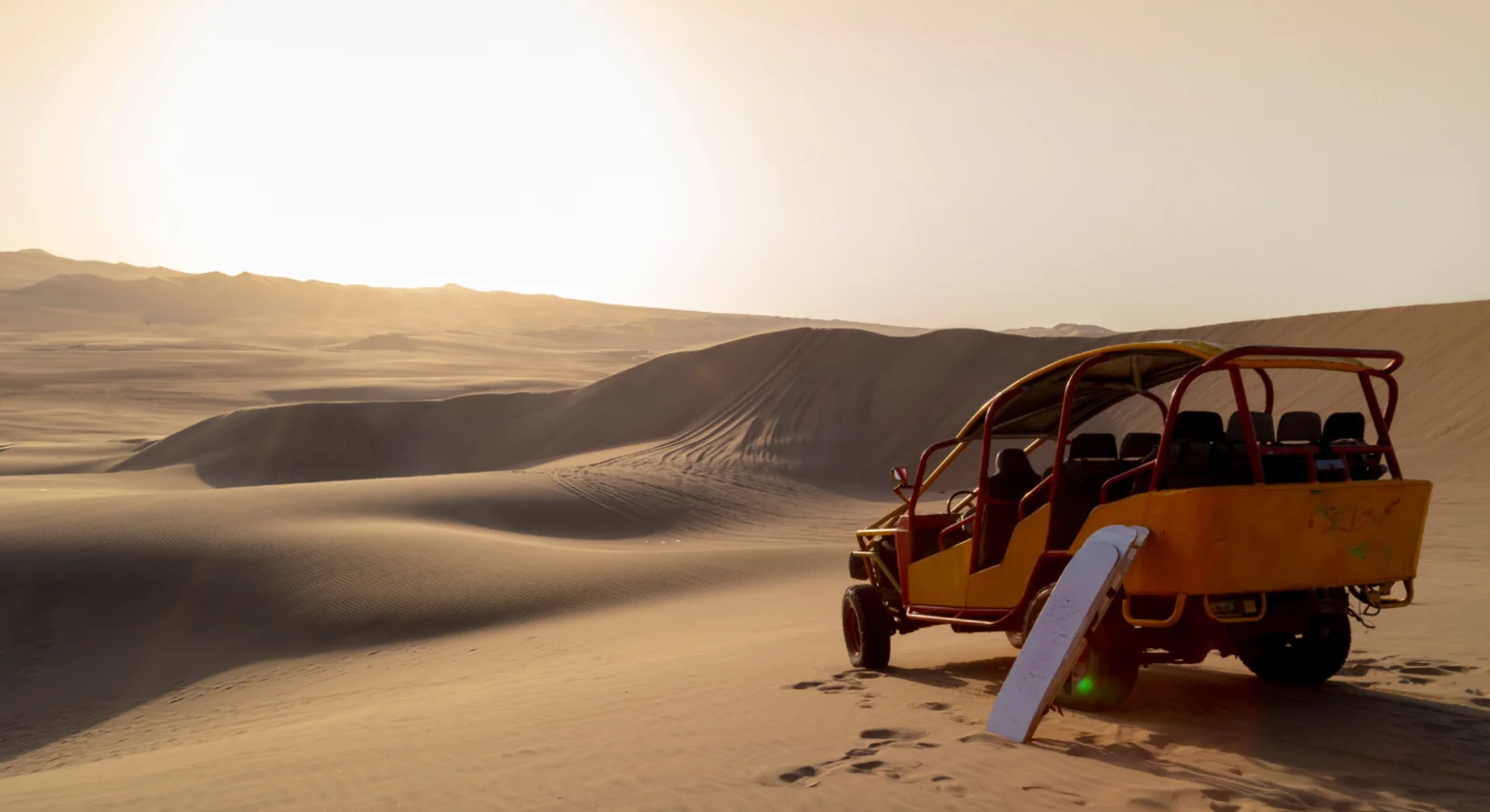 Dune buggy parked on desert sand dunes at sunset.