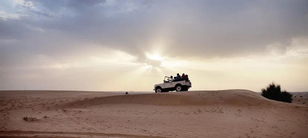 Visitors riding in an open 4x4 across the Liwa dunes at sunset