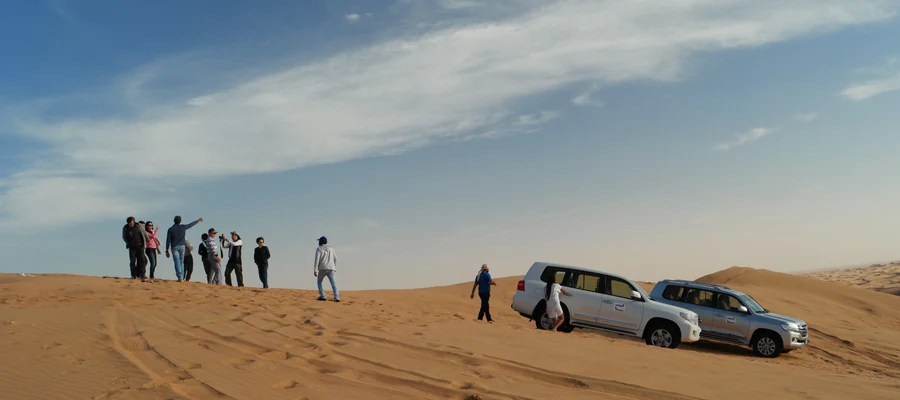 Tourists and SUVs on a sandy desert dune in Dubai.
