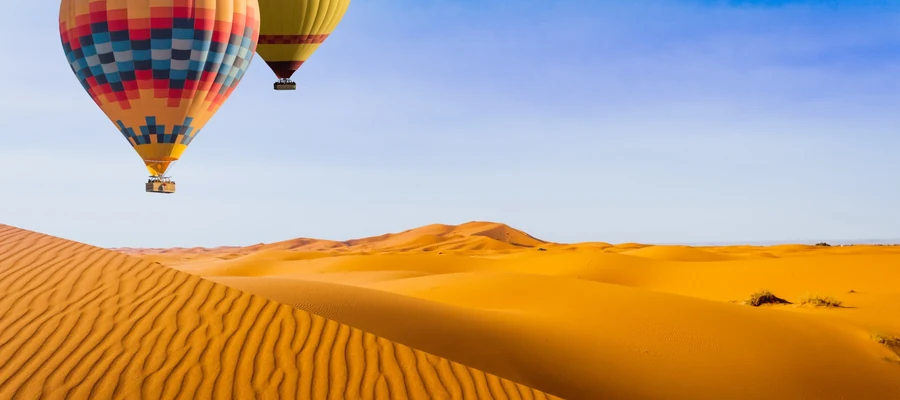 Two hot air balloons floating over the Dubai desert dunes at sunrise.