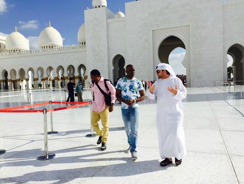 Male visitors wearing long trousers and a guide in a white kandura at Sheikh Zayed Grand Mosque