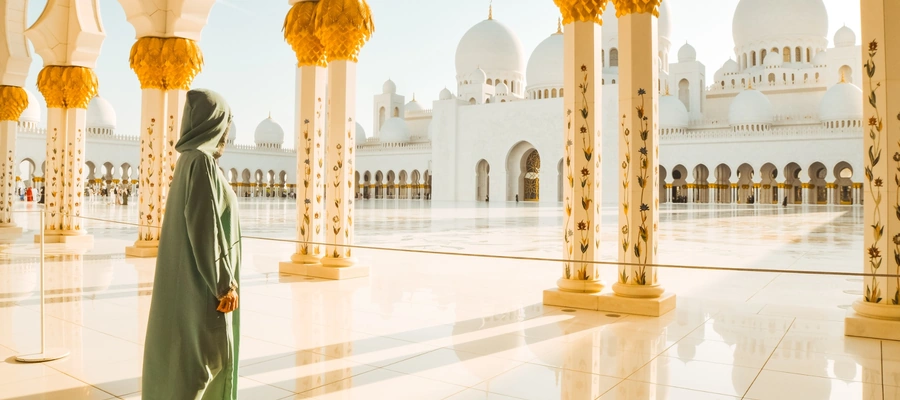 Woman in a green abaya and headscarf walking beside ornate columns at Sheikh Zayed Grand Mosque